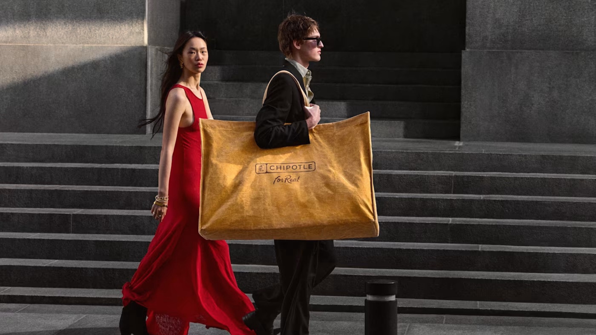 Two people walking together, with one carrying Chipotle's coveted Big Ass Bag.